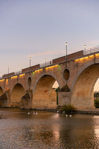 Arch bridge over river against sky during sunset