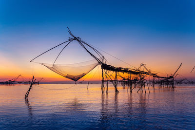 Fishing net by sea against sky during sunset