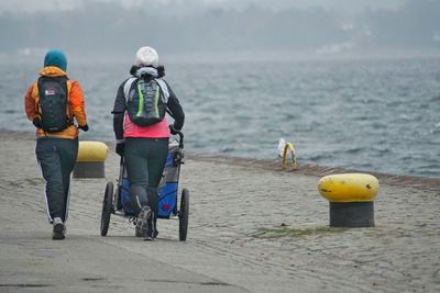 Rear view of people walking with baby carriage on pier