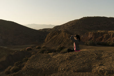 Woman siting with her hands on her eyes with mountains background