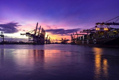 Cranes at commercial dock against sky at sunset