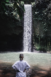 Rear view of woman looking at waterfall in forest