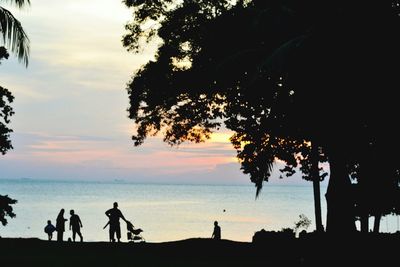 Silhouette people on beach against sky during sunset