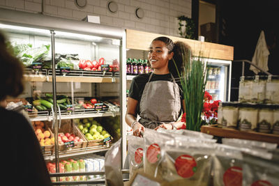 Smiling saleswoman looking at customer while standing in grocery store