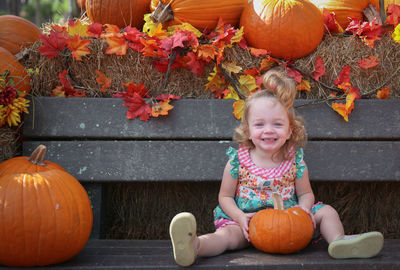 Full length of smiling girl with pumpkins in park during autumn