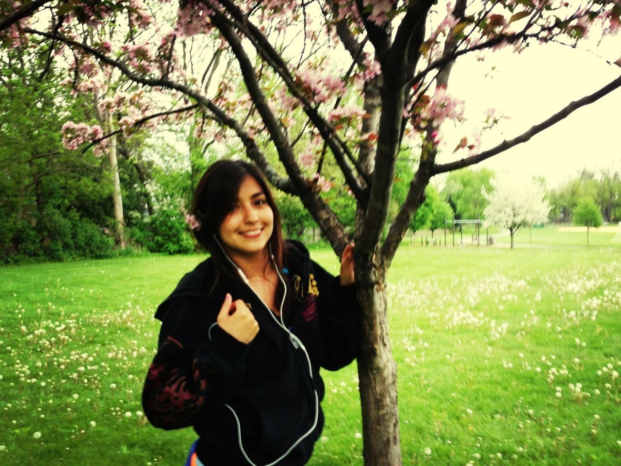 tree, grass, young adult, lifestyles, person, leisure activity, looking at camera, young women, casual clothing, portrait, smiling, front view, park - man made space, field, standing, green color, grassy, long hair