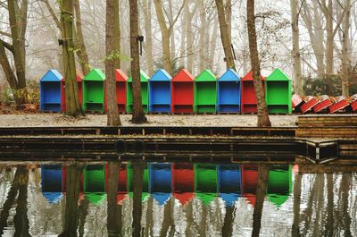 Multi colored chairs by lake against trees