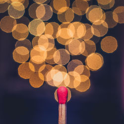 Close-up of matchstick against illuminated defocused lights at night