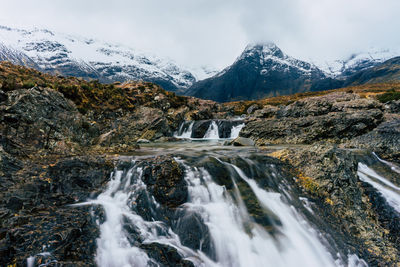 Scenic view of river flowing by snowcapped mountains against sky