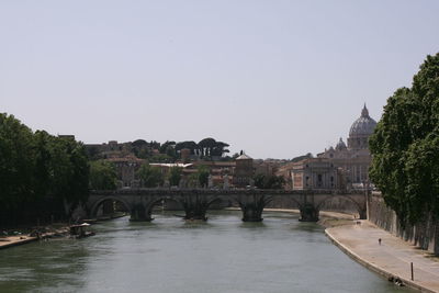 Bridge over river by buildings against clear sky