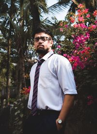 Portrait of young man wearing eyeglasses while standing against plants