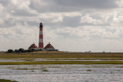 Lighthouse on field by building against sky