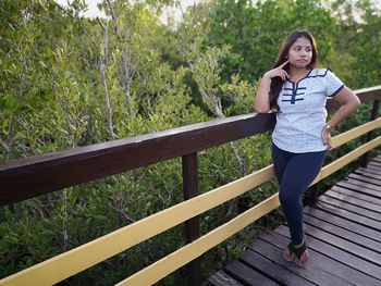 Full length of young woman standing by trees on boardwalk