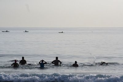 Silhouette swimmers enjoying in sea against clear sky