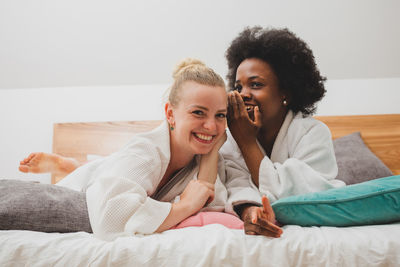 Woman whispering to friend lying on bed