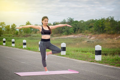 Full length of young woman doing yoga on road
