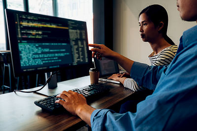 Midsection of man working with colleague on computer in office