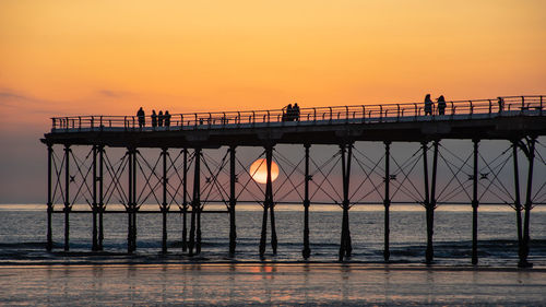 Silhouette people on bridge over sea against sky during sunset