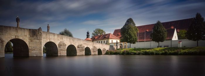Arch bridge over river amidst buildings against sky