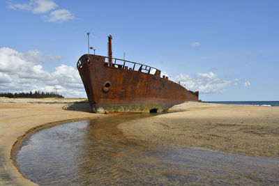 Abandoned boat on beach against sky