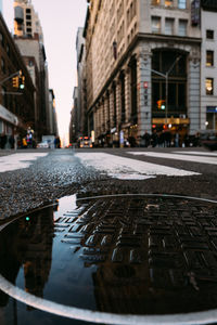 Manhole on wet road amidst buildings in city during rainy season