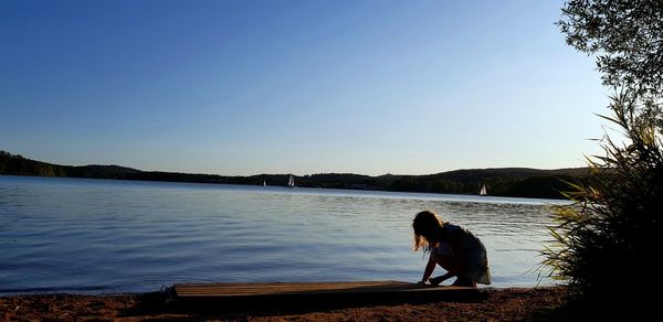 Man sitting on lake against clear sky