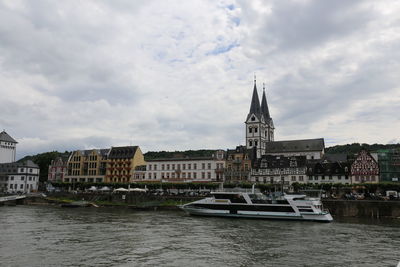 View of buildings by river against cloudy sky