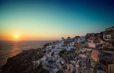 Aerial view of townscape by sea against clear sky during sunset