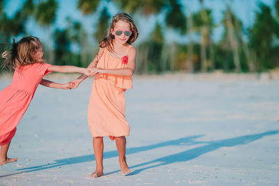 Full length of cute girls holding hands standing on beach