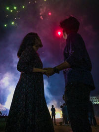 Rear view of couple standing against sky at night
