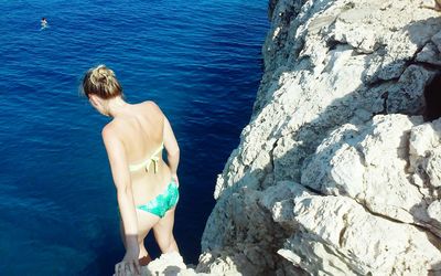 High angle view of sensuous woman in bikini standing on cliff against sea