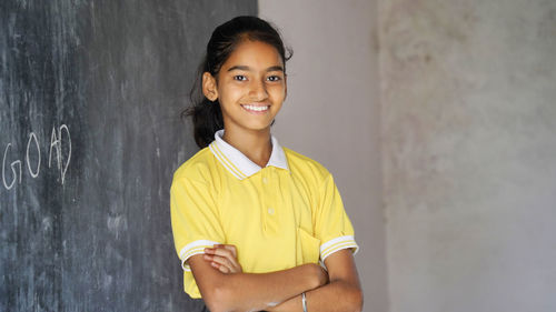 Happy indian school girl child standing in front of black chalkboard background. education concept