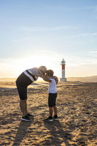 Full length of grandfather with grandson on beach against sky during sunset