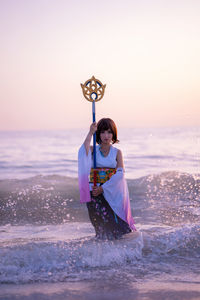 Woman standing in sea against sky during sunset