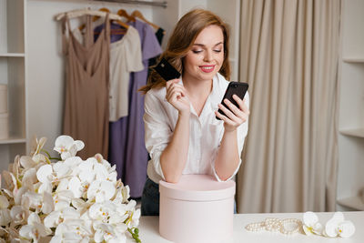 Girl holds a smartphone and a bank card against the background of the wardrobe