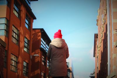 Rear view of person amidst buildings against sky