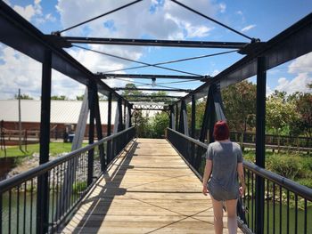 Rear view of woman in redhead walking on bridge during sunny day