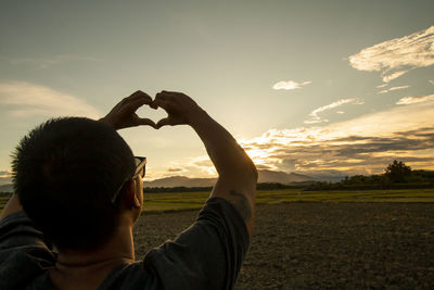 Rear view of man on field against sky during sunset