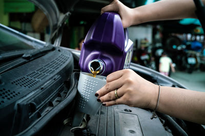 Cropped hand of woman pouring motor oil in garage