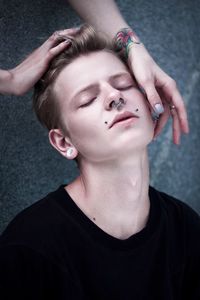 Cropped image of hands touching young man wearing nose ring against wall