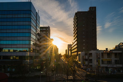 City street by buildings against sky during sunset