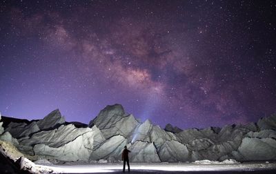 Man with flashlight standing against snowcapped mountain at night