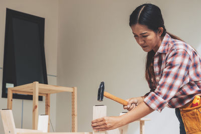 Young woman looking at camera while standing against wall at home