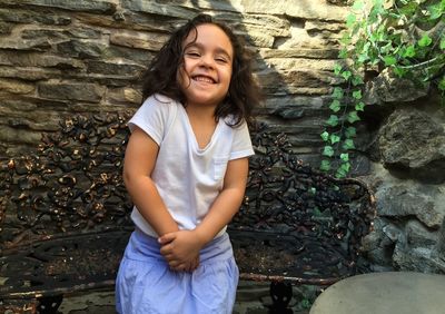 Cheerful girl sitting on bench against stone wall at outdoors cafe