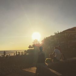 People relaxing on beach against sky during sunset