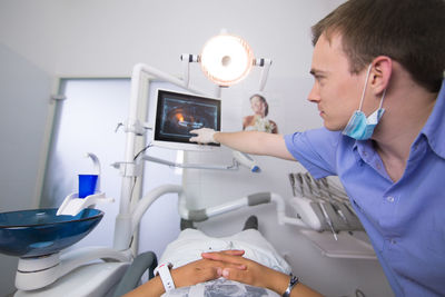 Doctor pointing at monitor with patient lying down at dentist office