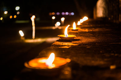 Close-up of burning diyas on retaining wall at night