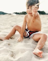 Shirtless boy spilling sand at beach