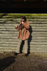 A young woman with a brown coat, posing in front of old wooden planks