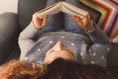 Woman reading book while lying on sofa at home